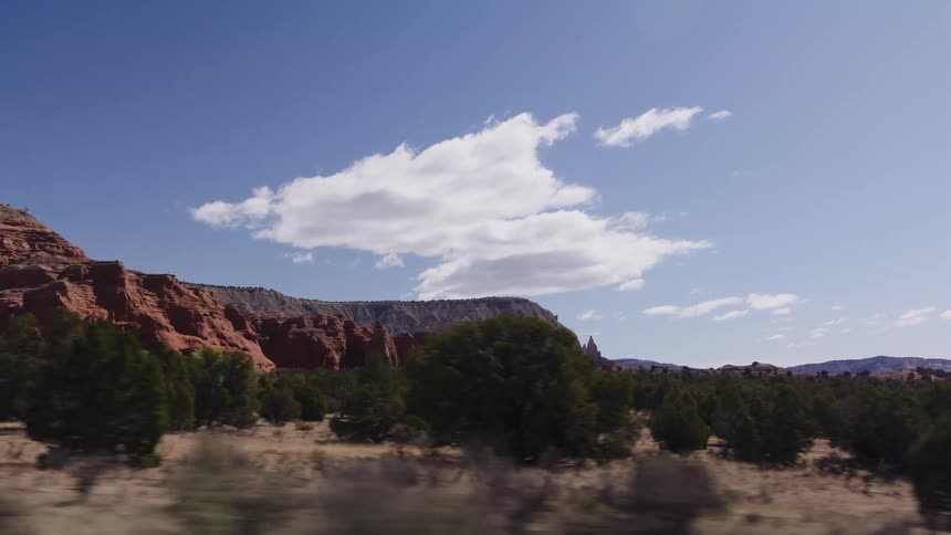 A scenic point-of-view drive through a desert canyon, passing majestic red rock formations under a brilliant blue sky