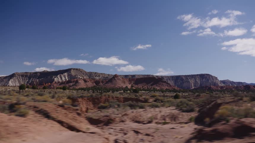 A scenic drive through a vast desert valley revealing colorful red rock formations under a bright blue sky