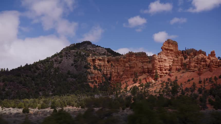 A scenic driving shot captures the stunning contrast of a forested mountain and vibrant red rock formations in Utah