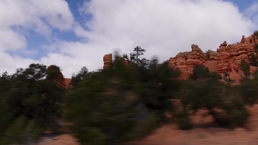 Passenger's point-of-view driving past the iconic red rock formations and pine trees of Red Canyon in Utah