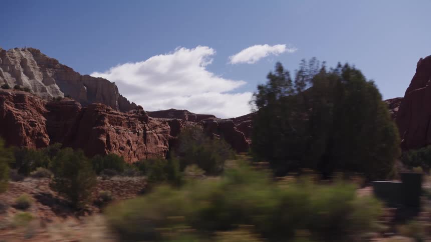 Driving past majestic red and white rock formations in a vast desert canyon under a clear blue sky