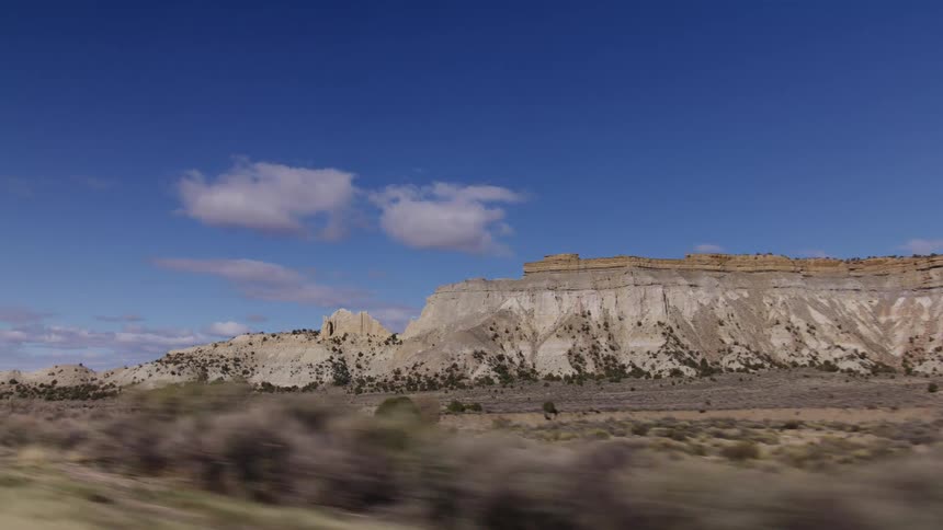 Driving past stunning layered rock formations and mesas in the vast desert badlands on a sunny day