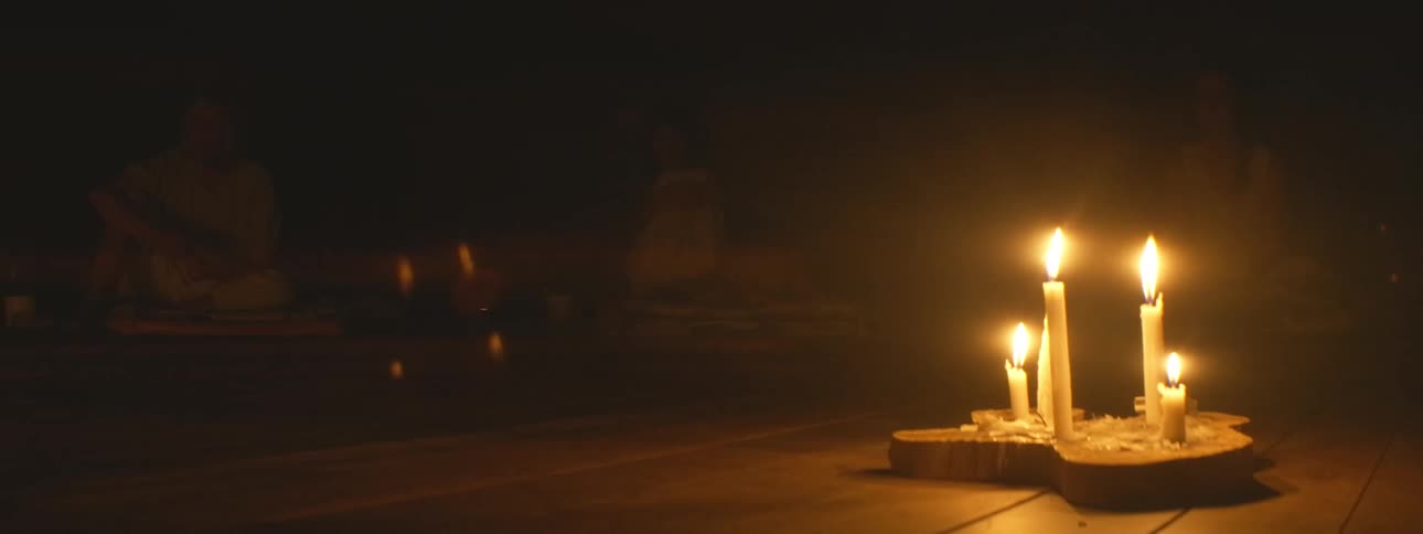Close up of burning candles illuminating a dark room where people are gathered for a peaceful meditation