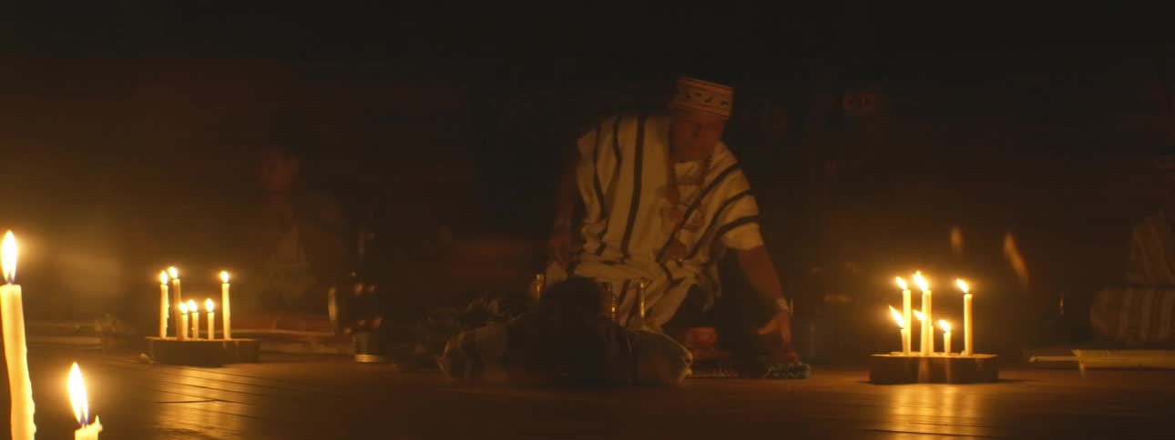 A traditional shaman leads a mystical healing ceremony by candlelight in a dark, sacred space