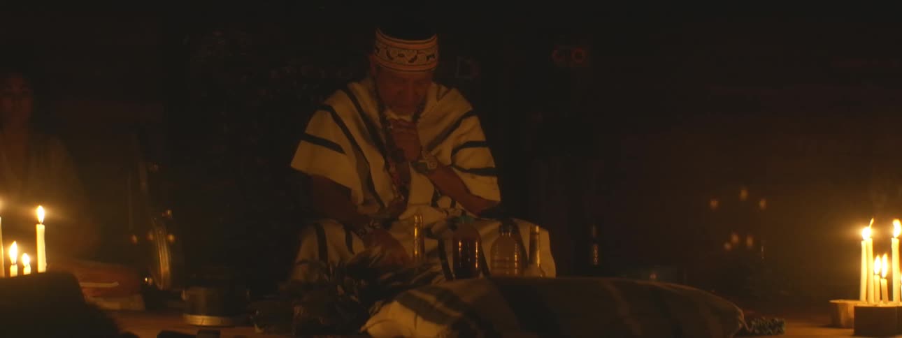 An indigenous shaman performs a spiritual ceremony by candlelight in a dark room
