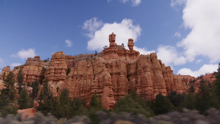 Driving alongside stunning red rock formations and hoodoos against a partly cloudy blue sky