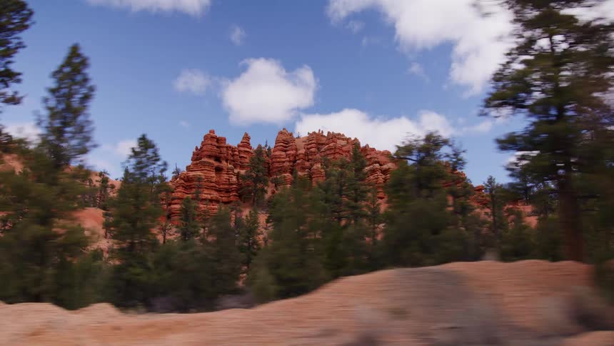 Driving along a scenic highway reveals the stunning red rock formations and evergreen trees under a partly cloudy sky