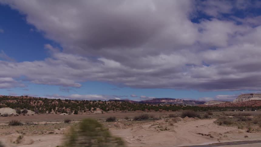 A scenic drive through a vast desert valley, passing rolling hills and scrubby trees under a dramatic, cloudy sky