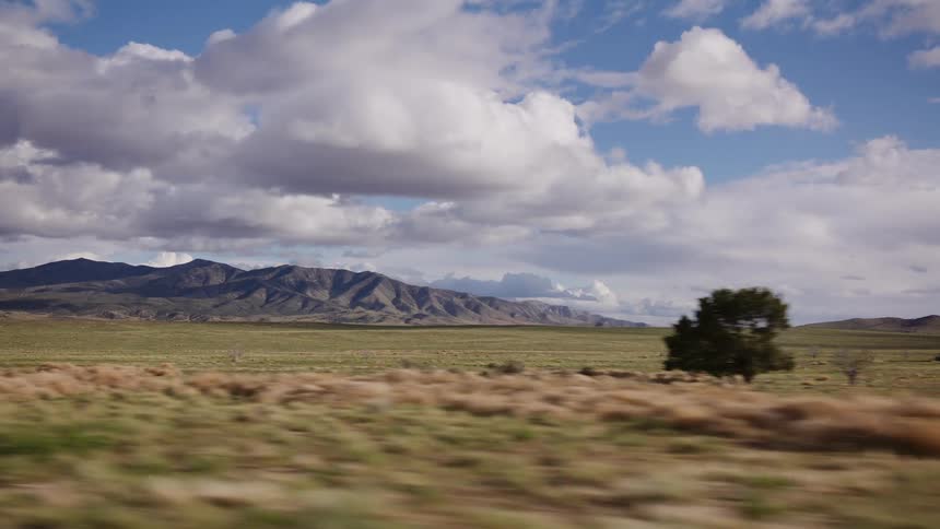 A scenic drive through a vast desert plain with distant mountains under a partly cloudy sky