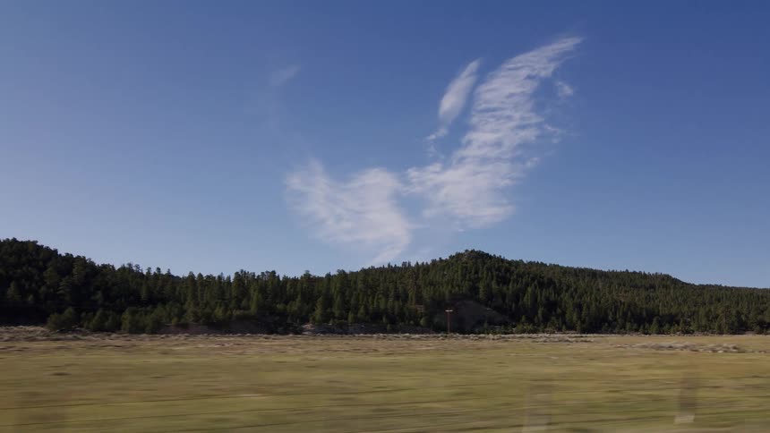 A scenic drive through a vast rural landscape with rolling green hills and a clear blue sky