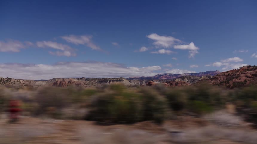 A scenic drive through the vast desert landscape of the American Southwest, passing by red rock mountains and arid plains under a blue sky