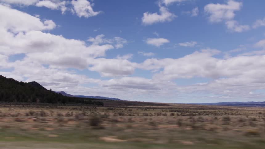 Driving plate shot of a vast prairie landscape with distant mountains under a bright blue sky with clouds