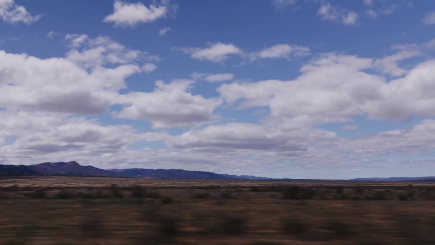Passing by the rugged, dry landscape of the outback with distant mountains under a beautiful cloudy blue sky