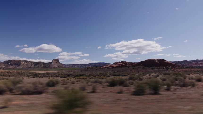 Driving past a stunning desert landscape with red rock formations and buttes under a blue sky in Utah