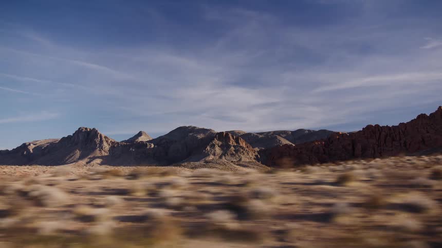 Driving past a vast, arid landscape of rocky mountains and desert scrub under a brilliant blue sky