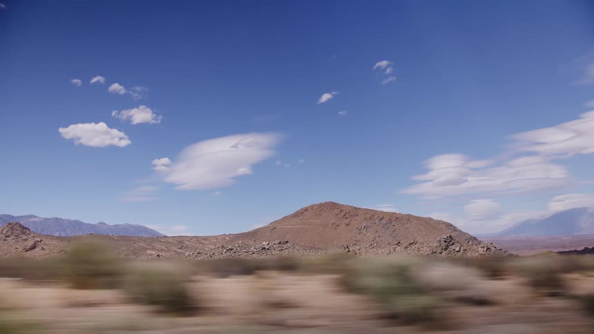 Driving shot of a barren desert landscape with rocky hills and a vibrant blue sky