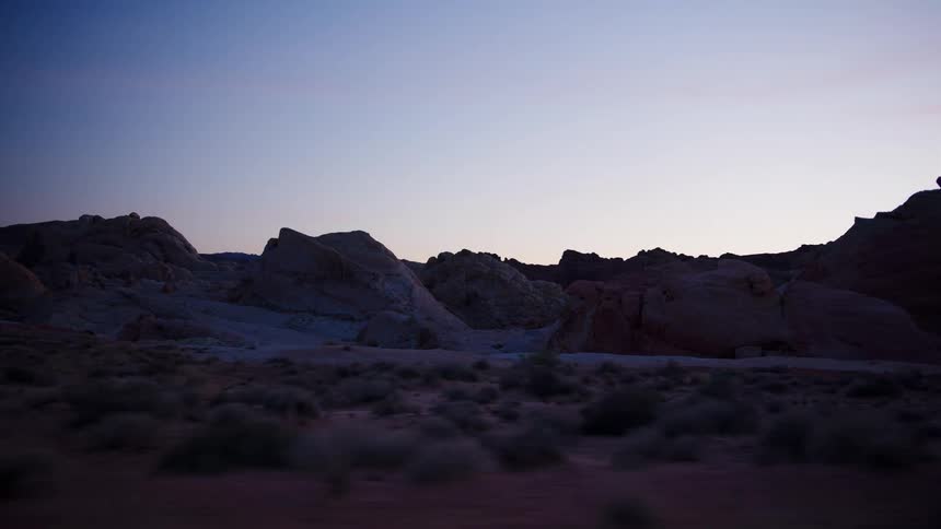A smooth side-tracking shot of a desolate desert landscape featuring unique rock formations at twilight
