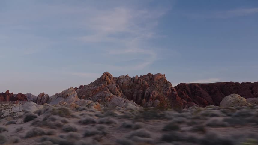A slow tracking shot glides through a desert landscape, revealing vibrant red and white rock formations against a clear dusk sky