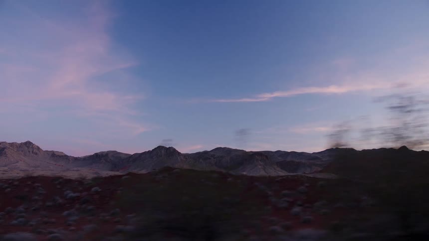 A scenic drive through a vast desert mountain landscape as the sky glows with the colors of sunset