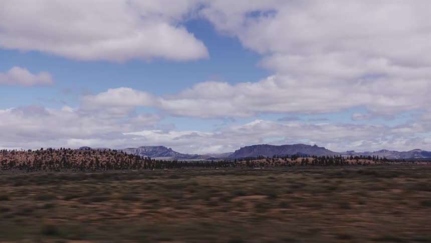 Driving through a vast, arid landscape with distant mountains under a partly cloudy blue sky