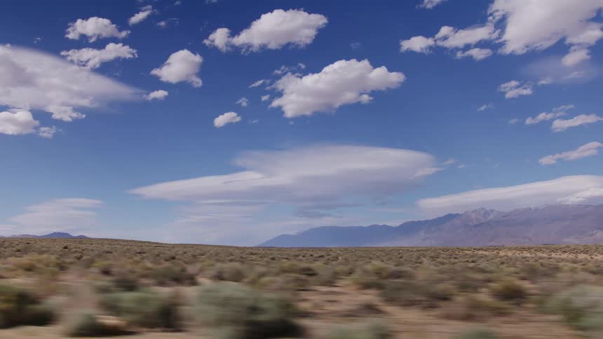 Driving plate shot of a vast desert landscape with distant mountains under a beautiful blue sky