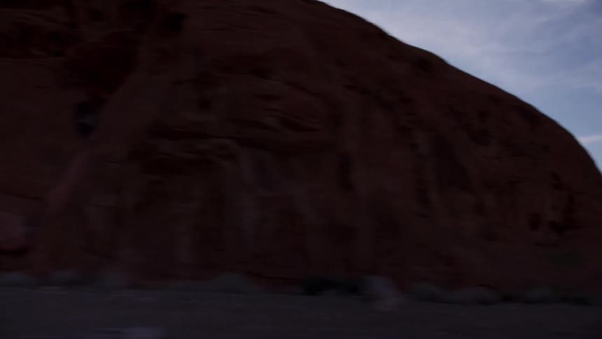 Driving past silhouetted red rock formations in a vast desert landscape as the sun hangs low in the sky