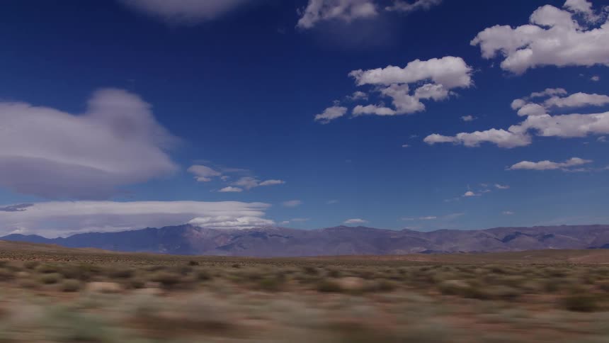 A scenic drive through an expansive desert valley with a majestic mountain range under a beautiful blue sky