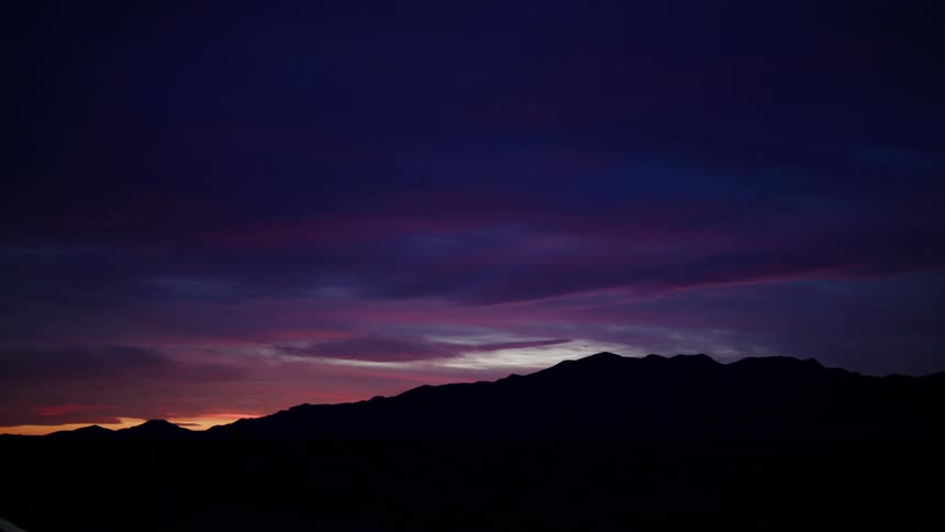 The last light of sunset creates a beautiful purple and pink sky over a silhouetted mountain range as seen while driving