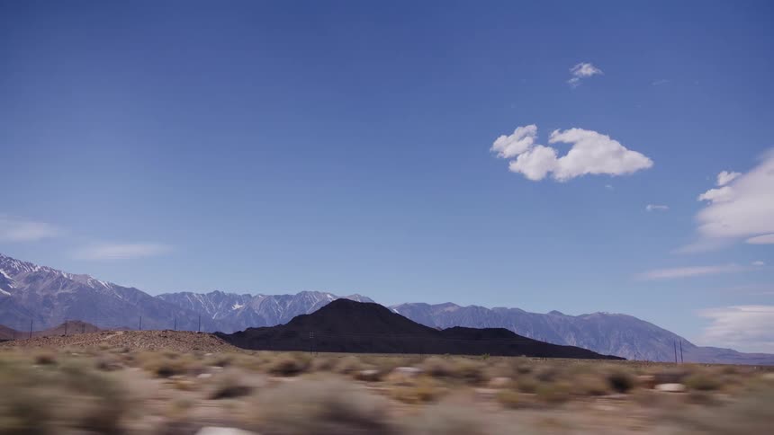 A scenic drive through a vast desert valley reveals a stunning view of snow-capped mountains under a clear blue sky