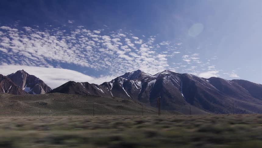 A scenic drive past majestic snow-covered mountains under a vast blue sky with fluffy white clouds