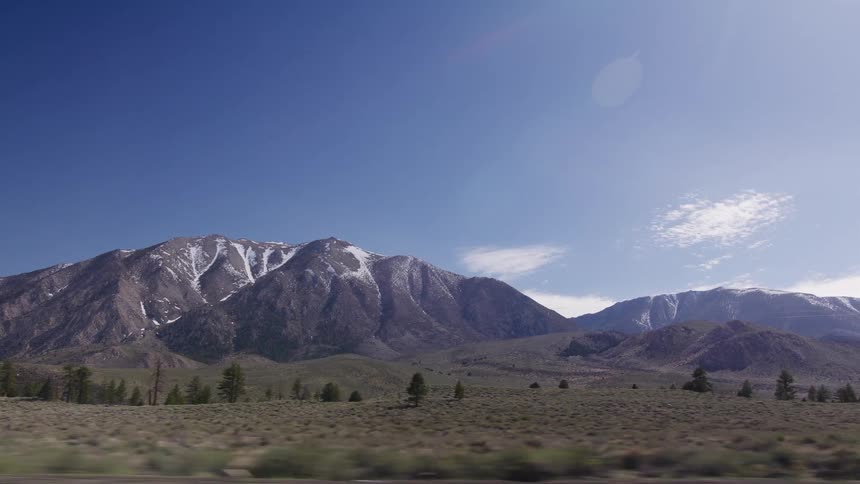 Scenic drive past a majestic snow-capped mountain range under a bright blue sky