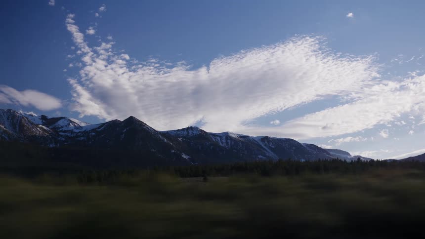 A scenic drive past majestic, snow-capped mountains and a pine forest under a vibrant blue sky
