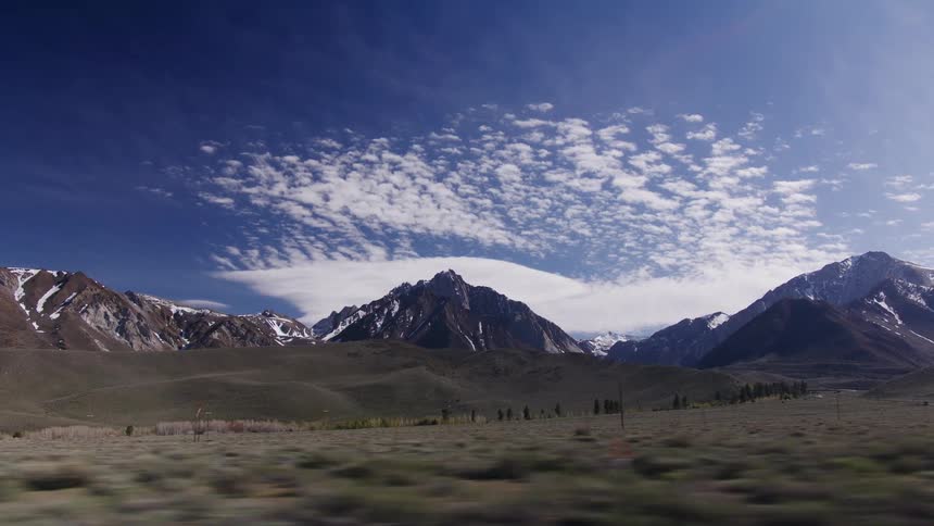 A scenic drive past majestic, snow-capped mountains and a vast valley under a beautiful blue sky