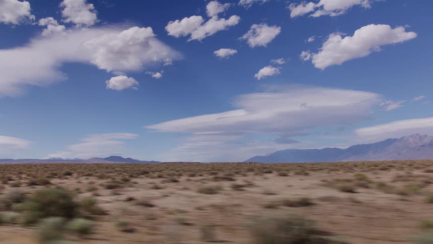 A scenic drive through a vast desert landscape, with distant mountains visible under a bright blue sky filled with white clouds