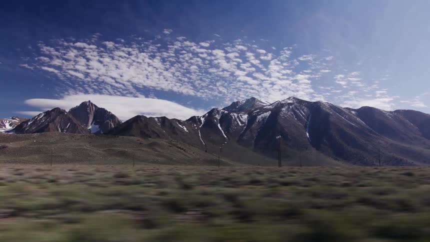 Side view from a moving car captures the snow-covered mountains of the Sierra Nevadas against a bright blue sky