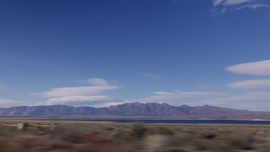 A scenic drive past a vast desert landscape, a serene blue lake, and a majestic mountain range under a wide-open sky
