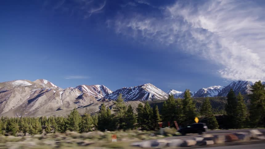 Driving past the majestic, snow-capped Sierra Nevada mountains on a clear day with a vibrant blue sky