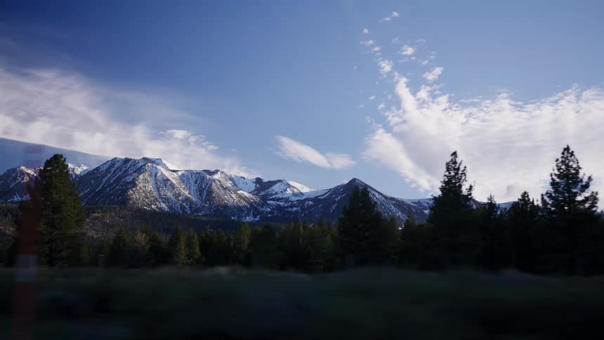 A scenic drive past majestic snow-covered mountains and evergreen forests under a bright blue sky