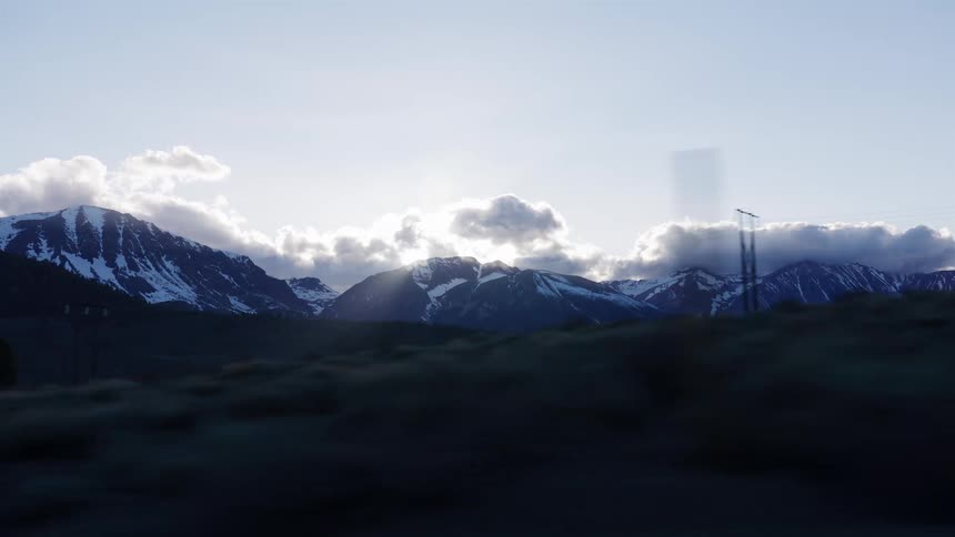 A scenic drive past a majestic snow-capped mountain range as the morning sun rises from behind the peaks