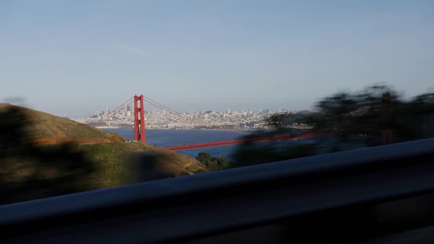 A wide, scenic driving plate shot of the iconic Golden Gate Bridge and the San Francisco skyline from the Marin Headlands