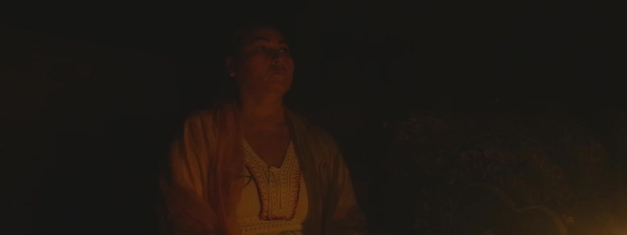A woman sits in quiet contemplation, her face illuminated by the warm glow of a flickering flame in the dark