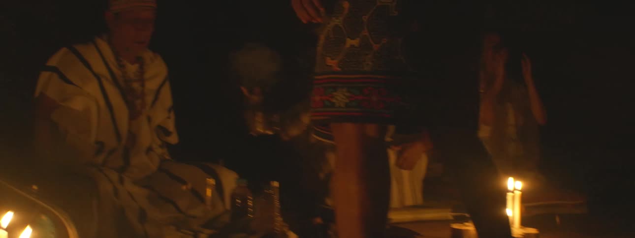 An indigenous shaman leads a traditional spiritual ceremony in a dark room lit by candlelight