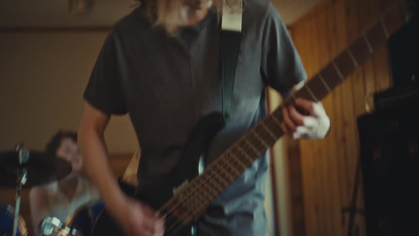 Teenage bass player with long hair gets into the groove while rehearsing with his band in a home studio