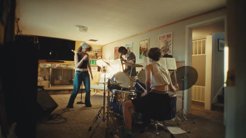A youthful rock band jams with raw energy in a home studio, the lead singer jumping wildly as they practice