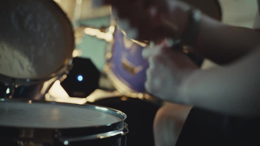 A close-up, out-of-focus shot of a drummer's hands playing a beat on a drum kit in slow motion
