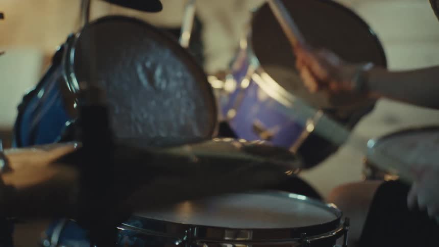 Slow-motion over-the-shoulder shot of a drummer's hands hitting the drums and cymbals with sticks