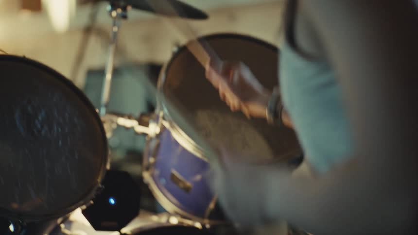 Slow-motion over-the-shoulder shot of a drummer's hands hitting the drums and cymbals with sticks