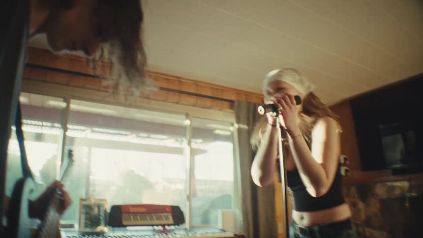 A young female singer and male bassist energetically rehearse their rock music in a cozy living room