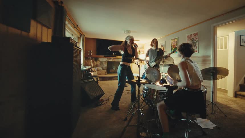 A young, energetic punk rock band rehearses in a basement, with a female singer, guitarist, and drummer passionately playing their music