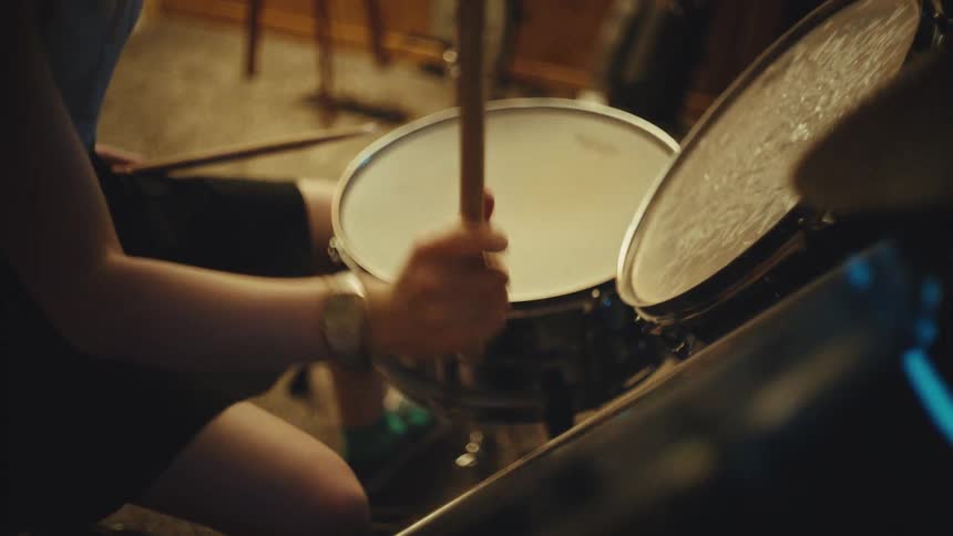 Female drummer energetically plays a drum kit in a cozy, vintage-style home music studio